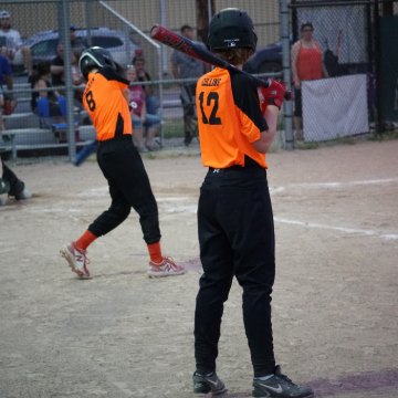 Two baseball players standing on the side of the baseball field practicing baseball bat swings.