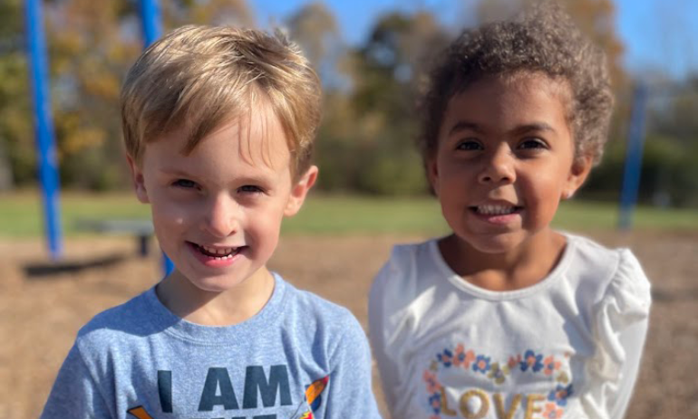 A young boy and a young girl are on the playground and they are smiling at the camera.