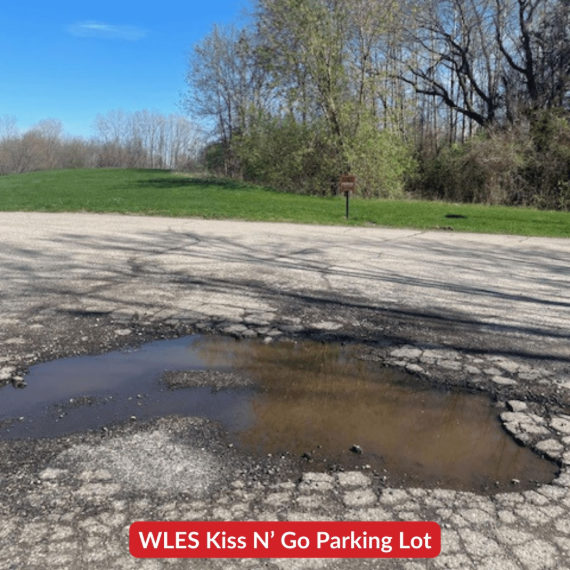 A large pothole filled with water in the Whitmore Lake Elementary School parking lot