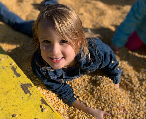 A young girl is smiling at the camer while playing in a sandbox.