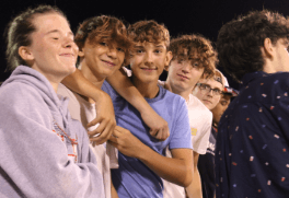 A group of young boys climbing on a rock climbing wall and smiling at the camera.