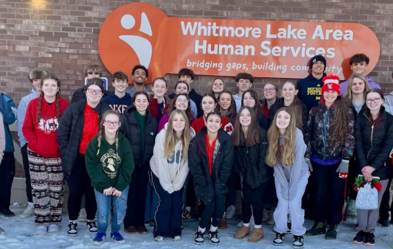 A group of students posing un front of a sign that says Whitmore Lake Area Human Services.