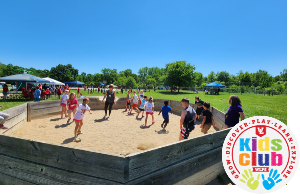 Three young girls stand in a classroom with their arms around each other while smiling at the camera.