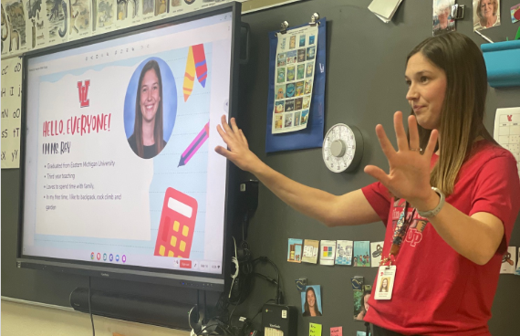 Two adult women stand behind a young girl and a young boy while smiling at the camera and posing in a classroom.